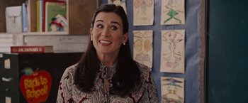 Movie still from “Talladega Nights: The Ballad of Ricky Bobby” (2006), directed by Adam McKay – A woman with long black hair standing in front of a wall of drawings; Close Up shot, Over the shoulder angle