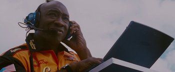 Movie still from “Talladega Nights: The Ballad of Ricky Bobby” (2006), directed by Adam McKay – An older man is talking on a cell phone and using a laptop computer; Close Up shot, Low angle