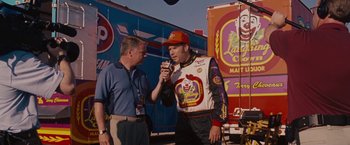 Movie still from “Talladega Nights: The Ballad of Ricky Bobby” (2006), directed by Adam McKay – A man is talking to a man in a racing suit; Medium shot, Over the shoulder angle
