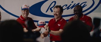 Movie still from “Talladega Nights: The Ballad of Ricky Bobby” (2006), directed by Adam McKay – A man in a red shirt is holding a hat; Medium shot, Over the shoulder angle