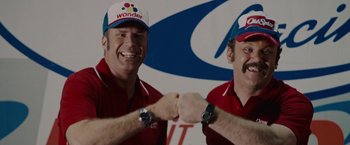 Movie still from “Talladega Nights: The Ballad of Ricky Bobby” (2006), directed by Adam McKay – A couple of men that are shaking hands in a room; Medium shot, Overhead angle