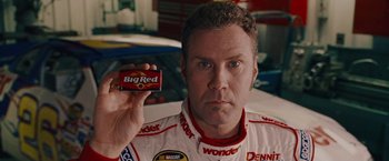 Movie still from “Talladega Nights: The Ballad of Ricky Bobby” (2006), directed by Adam McKay – A man holding a box of candy in front of him; Close Up shot, Over the shoulder angle