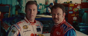 Movie still from “Talladega Nights: The Ballad of Ricky Bobby” (2006), directed by Adam McKay – A couple of men standing next to each other in a garage; Close Up shot, Over the shoulder angle