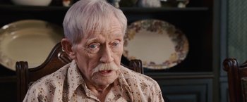 Movie still from “Talladega Nights: The Ballad of Ricky Bobby” (2006), directed by Adam McKay – An older man with white hair sitting in front of a table; Close Up shot, High angle