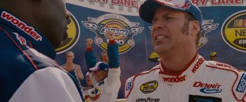Movie still from “Talladega Nights: The Ballad of Ricky Bobby” (2006), directed by Adam McKay – A group of people standing next to each other on a race track; Close Up shot, Low angle