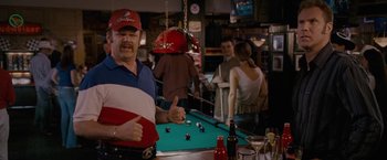 Movie still from “Talladega Nights: The Ballad of Ricky Bobby” (2006), directed by Adam McKay – A group of people standing around a pool table at a bar; Medium shot, High angle