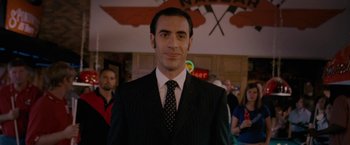 Movie still from “Talladega Nights: The Ballad of Ricky Bobby” (2006), directed by Adam McKay – A man in a suit and tie standing in front of a crowd of onlookers; Close Up shot, Low angle