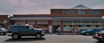 Movie still from “Talladega Nights: The Ballad of Ricky Bobby” (2006), directed by Adam McKay – A truck driving down a street past a store; Extreme Wide shot, Low angle