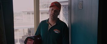 Movie still from “Talladega Nights: The Ballad of Ricky Bobby” (2006), directed by Adam McKay – A man wearing a red hat standing in front of a window; Medium shot, High angle