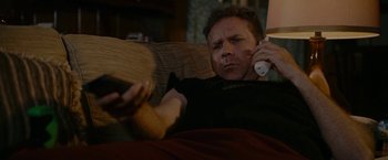 Movie still from “Talladega Nights: The Ballad of Ricky Bobby” (2006), directed by Adam McKay – A man sitting on a couch holding a remote control; Medium shot, High angle