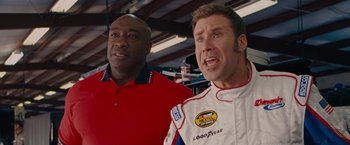 Movie still from “Talladega Nights: The Ballad of Ricky Bobby” (2006), directed by Adam McKay – Two men in red shirts and white racing suits; Medium shot, Over the shoulder angle