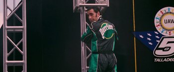 Movie still from “Talladega Nights: The Ballad of Ricky Bobby” (2006), directed by Adam McKay – A man in green and black racing suit standing next to a pole; Medium shot, Low angle