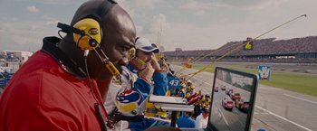 Movie still from “Talladega Nights: The Ballad of Ricky Bobby” (2006), directed by Adam McKay – A group of men sitting in the stands at a sporting event; Medium shot, Low angle