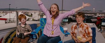 Movie still from “Talladega Nights: The Ballad of Ricky Bobby” (2006), directed by Adam McKay – A woman sitting on a chair with her arms raised; Medium shot, Low angle