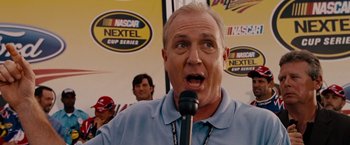 Movie still from “Talladega Nights: The Ballad of Ricky Bobby” (2006), directed by Adam McKay – An older man is speaking into a microphone; Close Up shot, Low angle