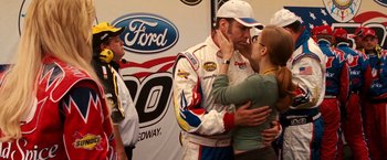 Movie still from “Talladega Nights: The Ballad of Ricky Bobby” (2006), directed by Adam McKay – A group of people hugging a race car driver; Medium shot, Over the shoulder angle