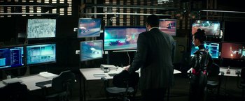 Movie still from “Teenage Mutant Ninja Turtles: Out of the Shadows” (2016), directed by Dave Green – A man standing in front of three computer monitors; Wide shot, Over the shoulder angle