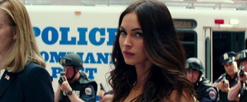 Movie still from “Teenage Mutant Ninja Turtles: Out of the Shadows” (2016), directed by Dave Green – A beautiful woman with long brown hair standing in front of a police sign; Close Up shot, Over the shoulder angle