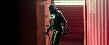 Movie still from “Teenage Mutant Ninja Turtles: Out of the Shadows” (2016), directed by Dave Green – A man in a black outfit holding a rifle; Wide shot, Low angle