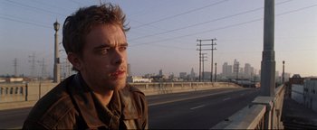 Movie still from “Terminator 3: Rise of the Machines” (2003), directed by Jonathan Mostow – A man standing next to a road with a city in the background; Close Up shot, Low angle