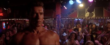 Movie still from “Terminator 3: Rise of the Machines” (2003), directed by Jonathan Mostow – A man with a muscular torso standing in front of a group of people; Medium shot, Low angle