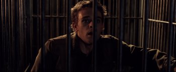 Movie still from “Terminator 3: Rise of the Machines” (2003), directed by Jonathan Mostow – A man standing behind bars in front of a fence; Close Up shot, High angle