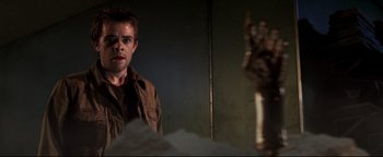 Movie still from “Terminator 3: Rise of the Machines” (2003), directed by Jonathan Mostow – A man standing next to a wall with his hand raised; Close Up shot, Low angle