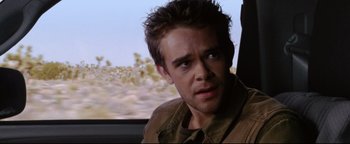 Movie still from “Terminator 3: Rise of the Machines” (2003), directed by Jonathan Mostow – A person with a car in the background; Close Up shot, Over the shoulder angle