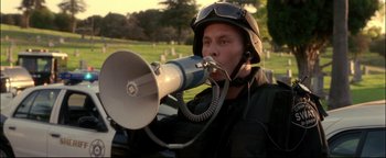 Movie still from “Terminator 3: Rise of the Machines” (2003), directed by Jonathan Mostow – A man in a helmet is holding a megaphone to his mouth; Medium shot, Low angle