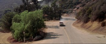 Movie still from “Terminator 3: Rise of the Machines” (2003), directed by Jonathan Mostow – A truck driving down a road near a forest; Extreme Wide shot, High angle