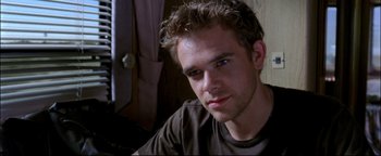 Movie still from “Terminator 3: Rise of the Machines” (2003), directed by Jonathan Mostow – A person sitting down looking at the camera; Close Up shot, Over the shoulder angle