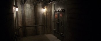 Movie still from “Terminator 3: Rise of the Machines” (2003), directed by Jonathan Mostow – An industrial looking room with a brick wall and a light fixture; Wide shot, High angle
