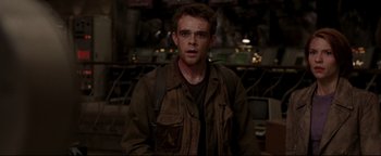 Movie still from “Terminator 3: Rise of the Machines” (2003), directed by Jonathan Mostow – A man in a brown jacket standing in front of a table; Close Up shot, Over the shoulder angle