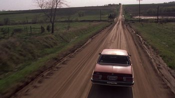 Movie still from “Terms of Endearment” (1983), directed by James L. Brooks – A car driving down a dirt road near a field; Extreme Wide shot, High angle