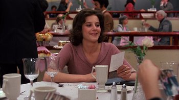 Movie still from “Terms of Endearment” (1983), directed by James L. Brooks – A woman sitting at a table holding a piece of paper; Medium shot, Over the shoulder angle