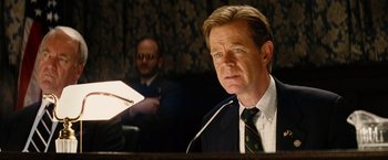 Movie still from “Thank You for Smoking” (2005), directed by Jason Reitman – A man in a suit and tie is sitting at a podium; Close Up shot, High angle