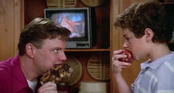 Movie still from “The 'Burbs” (1989), directed by Joe Dante – A man and a boy are eating a piece of food; Close Up shot, Over the shoulder angle