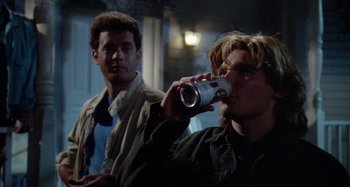 Movie still from “The 'Burbs” (1989), directed by Joe Dante – A man drinking a can of beer while another man watches; Medium shot, Low angle