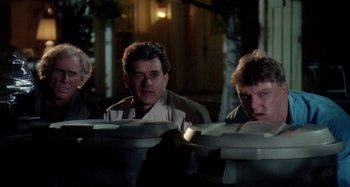 Movie still from “The 'Burbs” (1989), directed by Joe Dante – A group of people sitting at a table in front of a building; Medium shot, Low angle