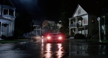 Movie still from “The 'Burbs” (1989), directed by Joe Dante – A car driving down a street at night with headlights turned on; Extreme Wide shot, Low angle