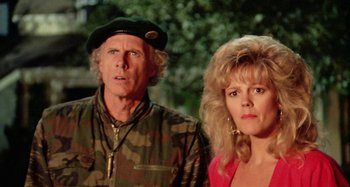 Movie still from “The 'Burbs” (1989), directed by Joe Dante – A man and a woman standing next to each other in front of trees; Close Up shot, Low angle