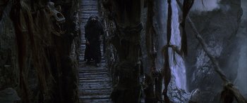 Movie still from “The 13th Warrior” (1999), directed by Michael Crichton – A man in a black robe walking down a wooden bridge; Wide shot, High angle