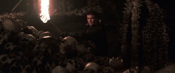 Movie still from “The 13th Warrior” (1999), directed by Michael Crichton – A man holding a sword standing in a pile of skulls; Medium shot, High angle