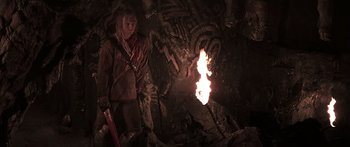 Movie still from “The 13th Warrior” (1999), directed by Michael Crichton – A person standing in a cave with a fire in the background; Wide shot, High angle