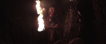 Movie still from “The 13th Warrior” (1999), directed by Michael Crichton – A man with a sword and a fire torches in the dark; Medium shot, Low angle
