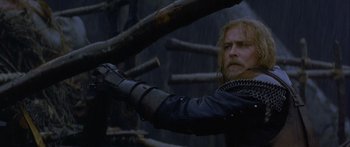 Movie still from “The 13th Warrior” (1999), directed by Michael Crichton – A man in a leather jacket holding a wooden stick; Medium shot, Low angle