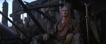 Movie still from “The 13th Warrior” (1999), directed by Michael Crichton – A statue of a man in chains with a man in chains; Medium shot, Low angle