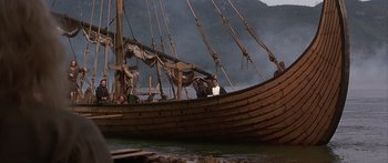 Movie still from “The 13th Warrior” (1999), directed by Michael Crichton – A man sitting on the side of a wooden boat in the water; Extreme Wide shot, High angle