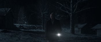 Movie still from “Out Stealing Horses” (2019), directed by Hans Petter Moland – A man standing in the dark holding a flashlight; Medium shot, Over the shoulder angle
