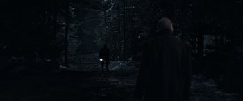 Movie still from “Out Stealing Horses” (2019), directed by Hans Petter Moland – A man is standing in the woods at night with a flashlight; Wide shot, Over the shoulder angle